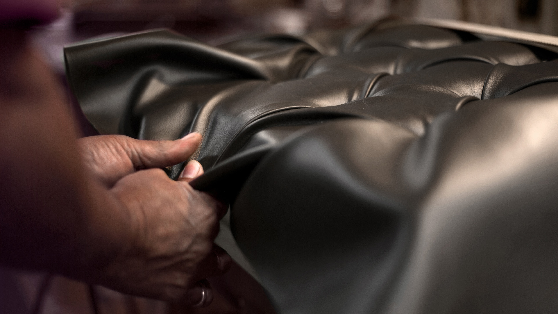 Man's hands stretching leather for quilted artist piano bench